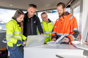 A survey team in high-visibility gear reviewing inspection records on board